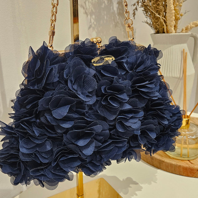 Bolso Miss azul con detalles florales, cadena dorada, diseño elegante sobre fondo decorativo.