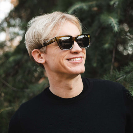 Joven feliz usando gafas de sol Hanukeii® Noosa Green / Black entre la naturaleza.