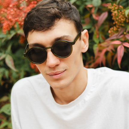 Hombre con gafas de sol Hanukeii® Harbor Green / Black en un entorno natural con plantas coloridas.